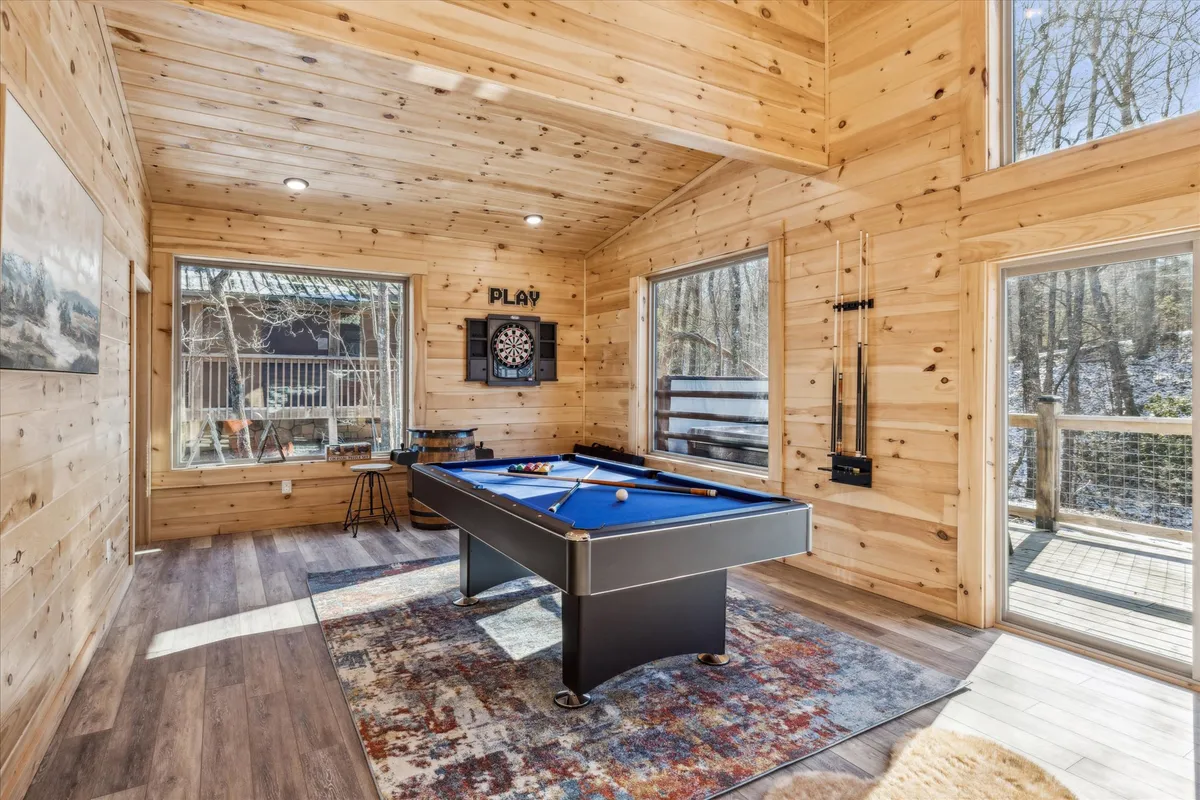 This interior image highlights the cabin’s recreational amenities, featuring a pool table and dart board framed by large windows and wooden walls. The setting is bright and inviting, suggesting fun and friendly competition.