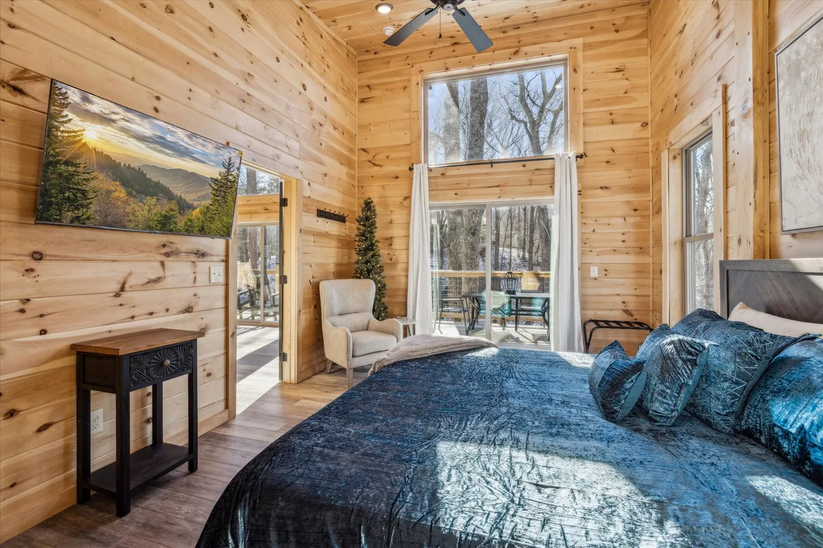 A plush bed adorned with decorative pillows sits beside large windows that let in natural light and offer scenic views. The wooden wall paneling and tranquil palette create a serene, high-end retreat ideal for relaxation.