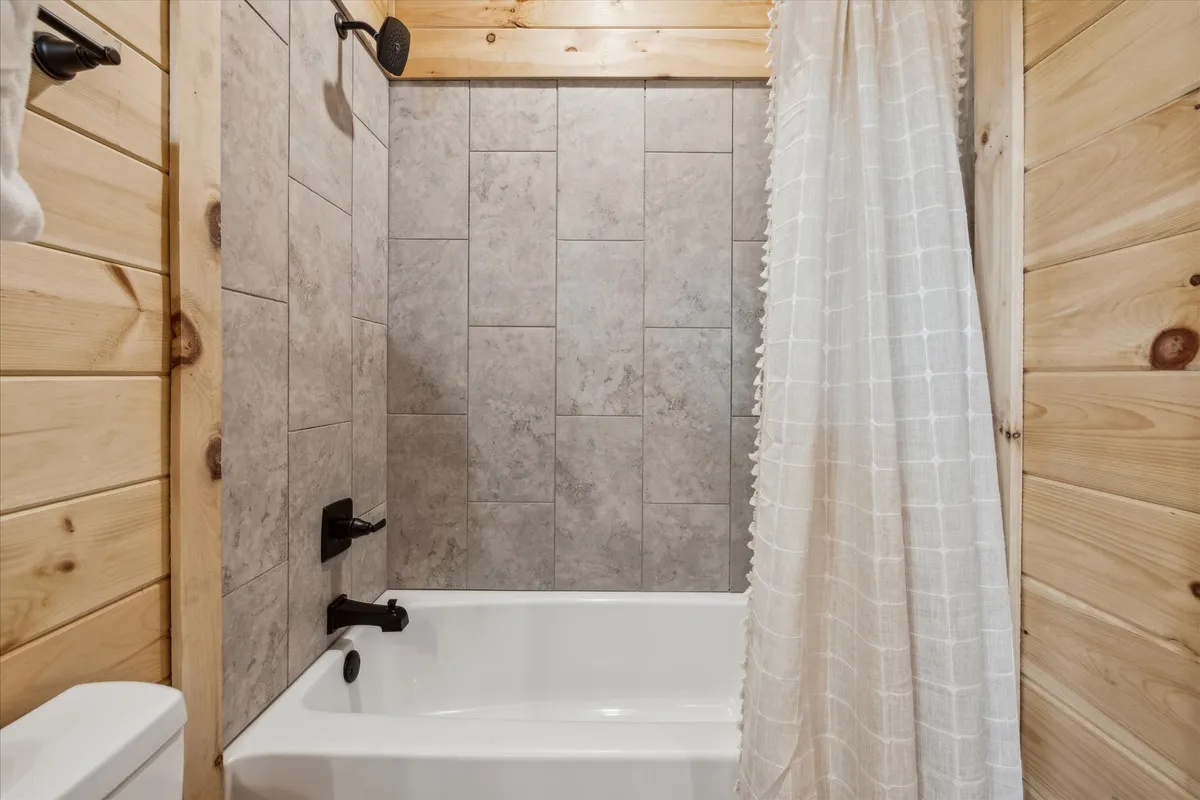 A bright, inviting bathroom featuring a bathtub, showerhead, warm wooden walls, and soothing tile details. The calm, tranquil mood invites guests to enjoy a relaxing soak or a refreshing shower.