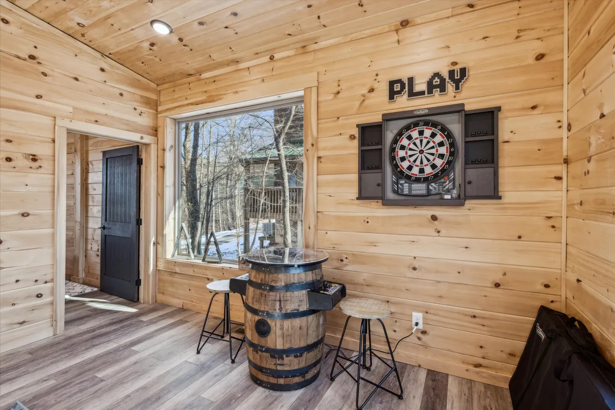 This image highlights a dartboard mounted on a wooden wall, with a barrel table below and a large window nearby. The setup encourages playful competition and socializing, with natural light streaming in and adding to the lively, relaxed vibe of the space.