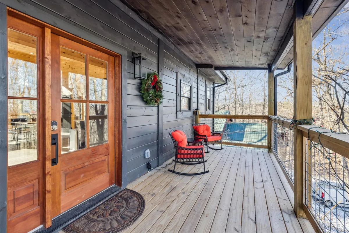 This exterior image showcases a welcoming wooden front door framed by rustic rocking chairs and a festive holiday wreath. The porch setting hints at relaxation and social interaction, connecting guests with the peaceful mountain environment and the idea of making memories together.