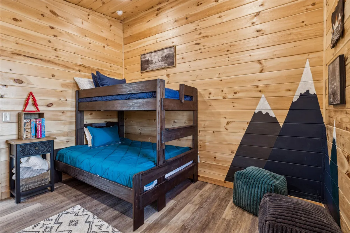 A playful yet comfortable bedroom with a bunk bed, a whimsical mountain mural, and a cozy nightstand. The room is perfect for children or friends, balancing fun and function, and adding variety to the sleeping options available.