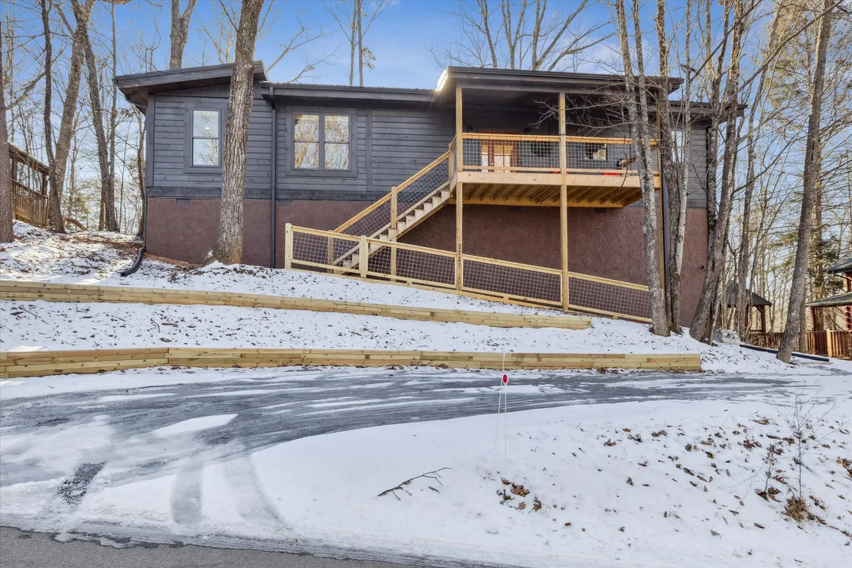 This image depicts a wooden deck set among tall trees, with a staircase leading to the entrance and a snow-covered ground visible below. The area exudes a peaceful, natural vibe and highlights the cabin’s integration with its surroundings.